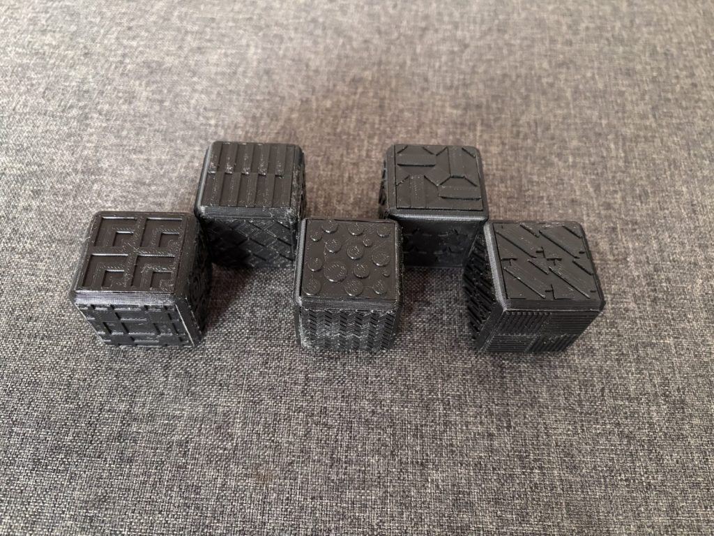 La face correspondant à "des enfants" se compose d’un motif répétitif complexe sans limite sur la face - il se coupe car la fin de la face s’y trouve mais il continuerait sinon. Ce motif est constitué de lignes diagonales en relief entre lesquelles se trouves des carrés qui ne se touchent pas. La face correspondant à "un husky" se compose de plusieurs triangles en relief formant un motif complexe. Celui-ci s’apparente à une alternance carrés constitués de deux triangles disposés côte à côte puis de deux triangles disposés l’un en face de l’autre et enfin à nouveau deux triangles côte à côte mais symétriques aux deux premiers. Les carrés sont similaires mais subissent une rotation de 90° par rapport au précédent (ils sont donc en damier mais subissent cette rotation). La face correspondant à "un vieil inuit" se compose de quatre carrés disposés dans les quatre coins. Chaque carré est constitué d’une alternance entre une ligne diagonales en relief et une ligne diagonale plate. Il se trouve trois lignes pleines (dont une au centre dont les deux extrémités sont coupées en formant un carré) et deux lignes vides dans chaque carré. La face correspondant à "un ours polaire" se compose de quatre carrées disposés dans les quatre coins. Chaque carré est une alternance de fines lignes en creux et de lignes plates. Les deux carrés inférieur droit et supérieur gauche se constituent de lignes verticales tandis que les deux carrées inférieur gauche et supérieur droit se constituent de lignes horizontales. La face correspondant à "un douanier" se compose de quatre carrées disposés dans les quatre coins. Chaque carré est constitué d’une alternance entre une ligne diagonales en relief et une ligne diagonale plate. Il se trouve cinq lignes pleines et quatre lignes vides dans chaque carré. La face correspondant à "un trader" se compose d’un motif complexe se répétant. Ce motif est constitué de reliefs en formes de gouttes d’eau qui se font face en des colonnes complètes. Il se trouve six colonnes sur la face.