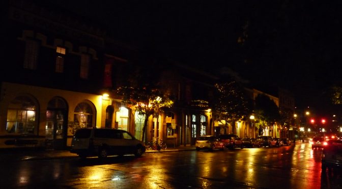 Picture of a street in a town at night, lit by lamp posts