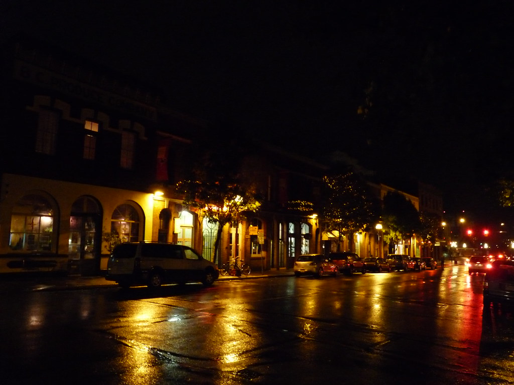 Picture of a street in a town at night, lit by lamp posts